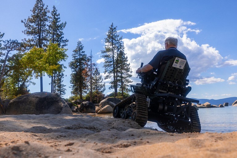 A man in a trackchair on a beach.