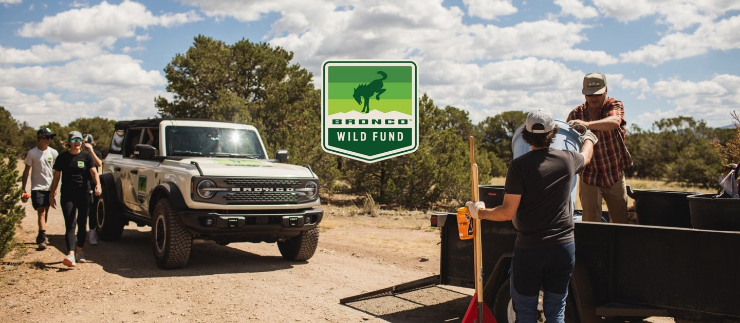 People unloading supplies from a trailer. Bronco Wild Fund logo with bucking horse. 