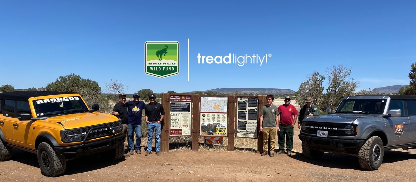 Six volunteers standing next to Bronco® SUVs and park signage