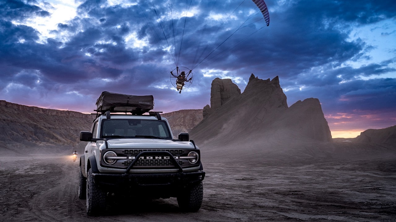 Front shot of a Bronco® SUV with a person flying a powered paraglider in the background