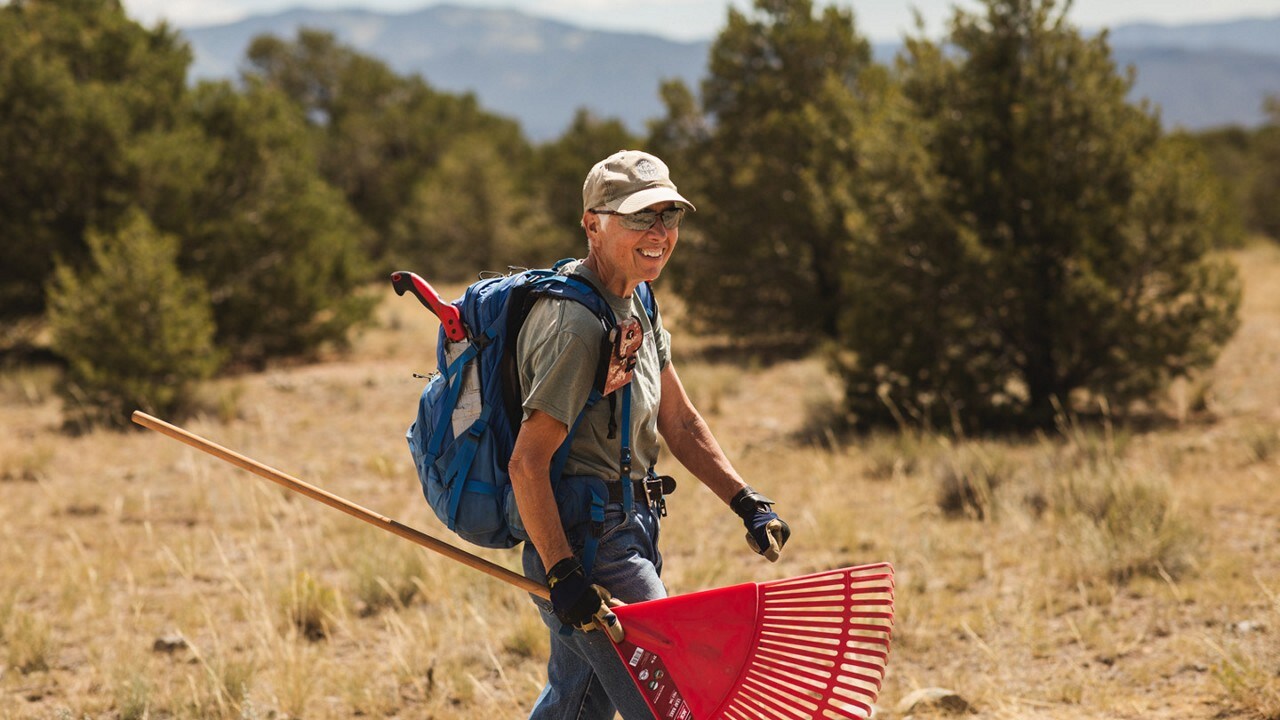 Volunteer wearing a backpack and holding a rake