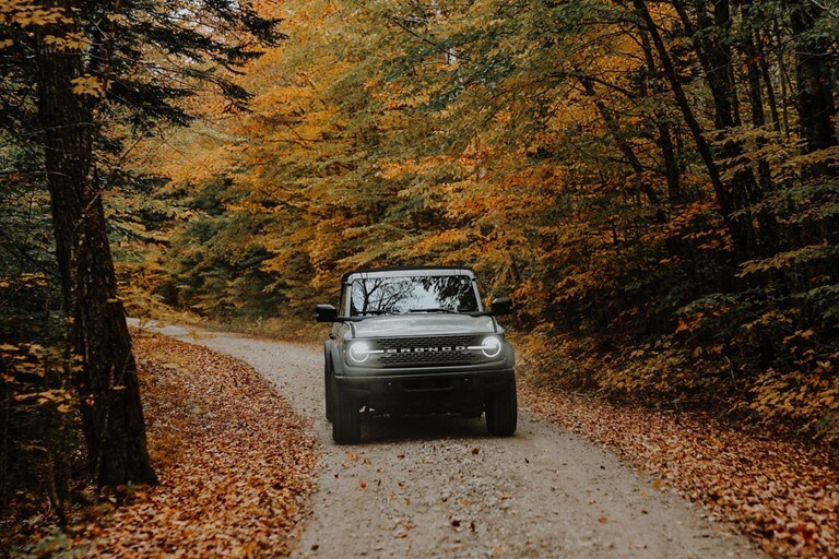 A Bronco® SUV being driven on a road with fall foliage.