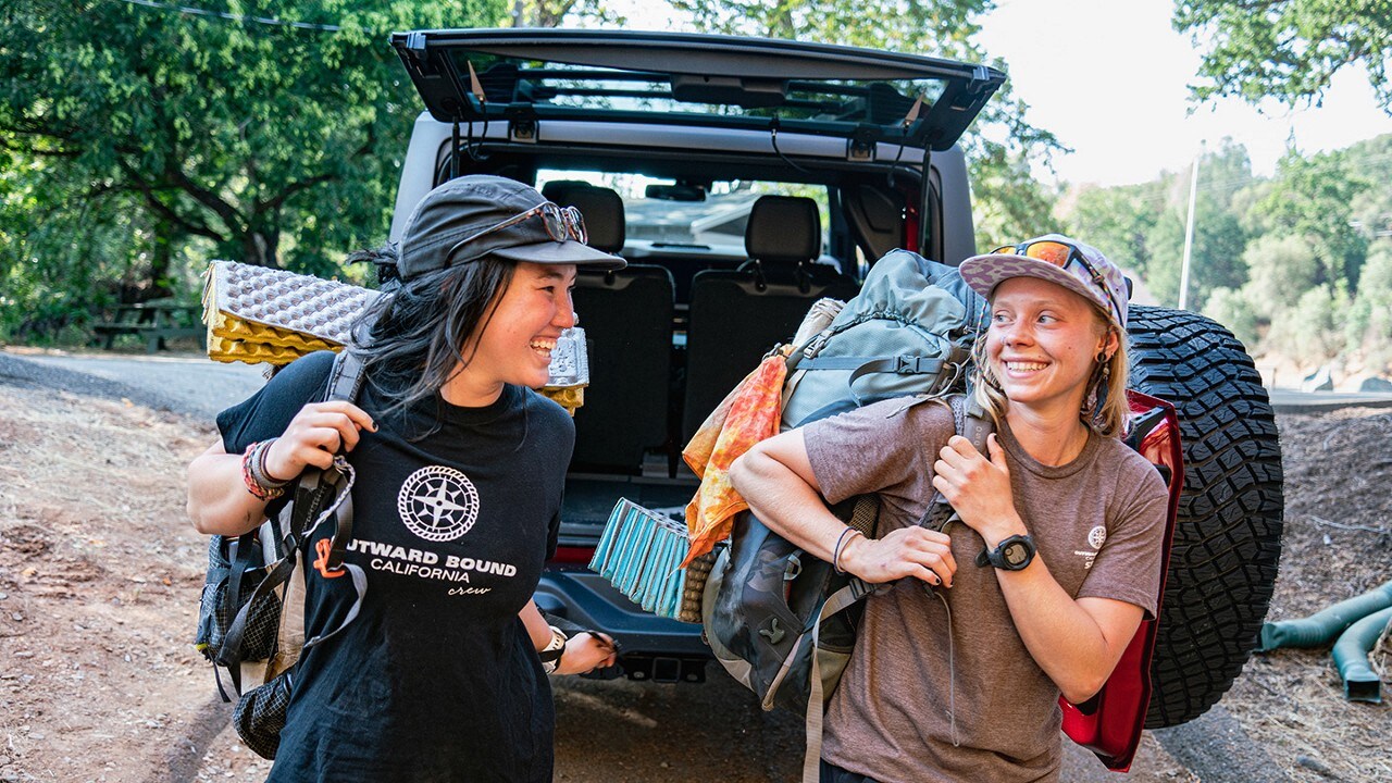 Two Outward Bound students walking with hiking equipment