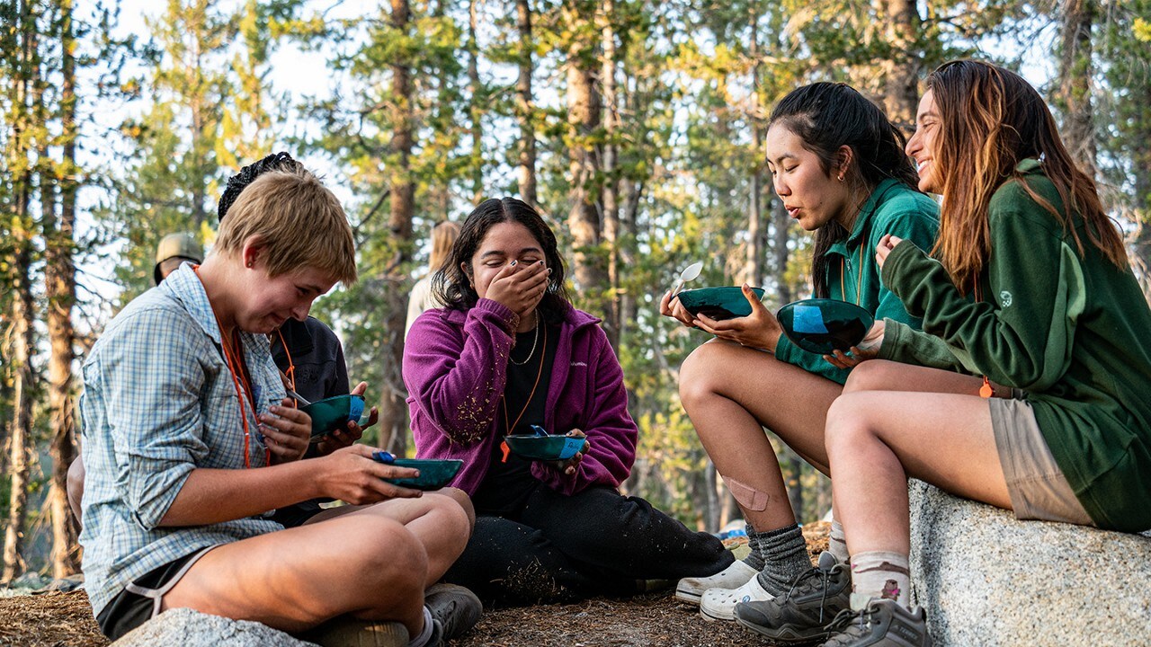 Group of Outward Bound students sitting on the ground eating and laughing