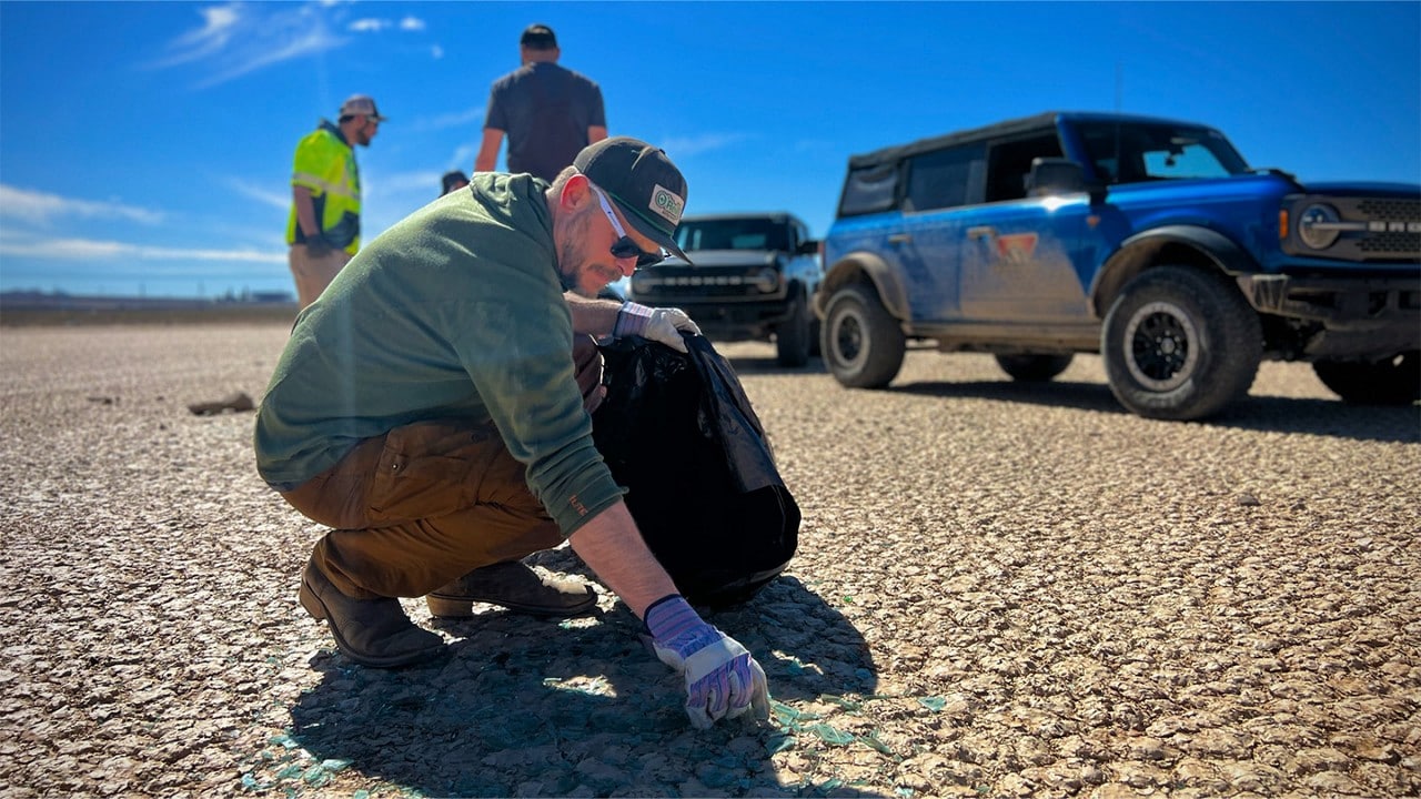 Volunteer picking up broken glass in a desert