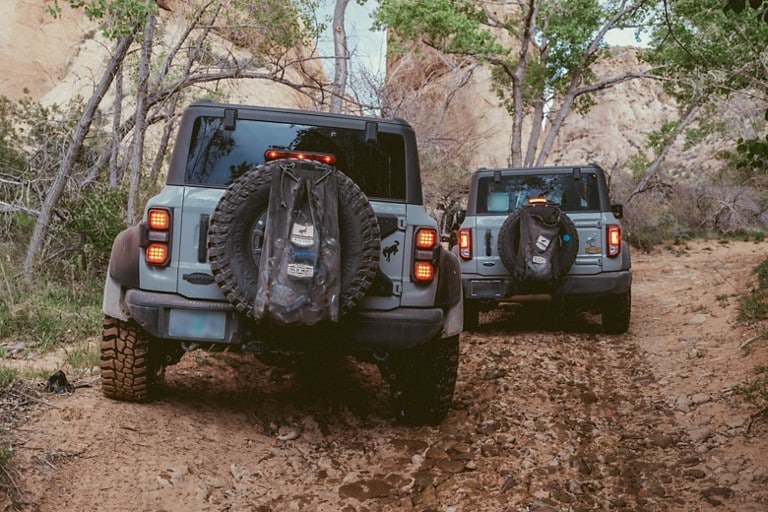 Two Bronco® SUVs on a trail with spare tire trash bags. 