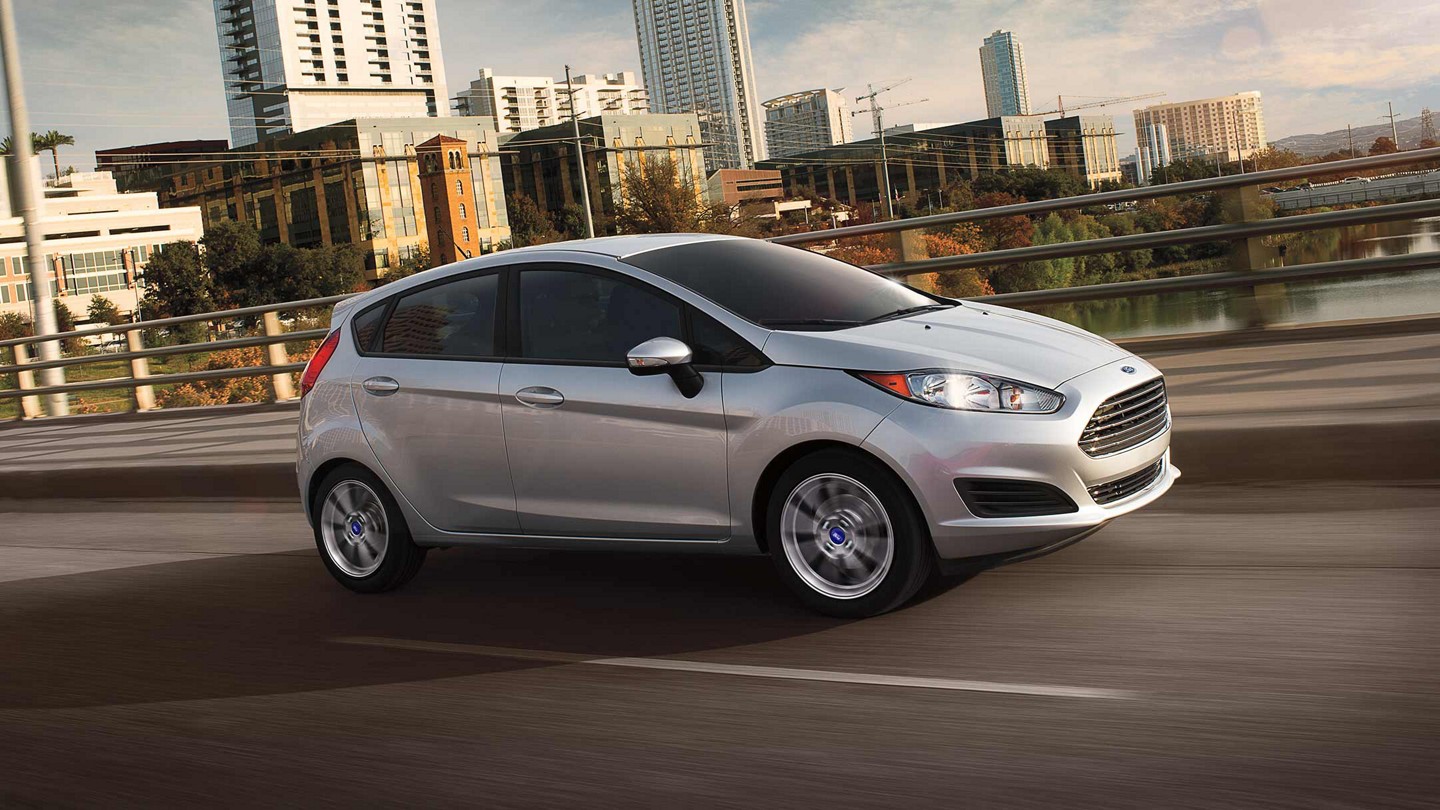 Ford Fiesta SE 5-door in Ingot Silver Metallic being driven over a bridge with a city skyline in the background