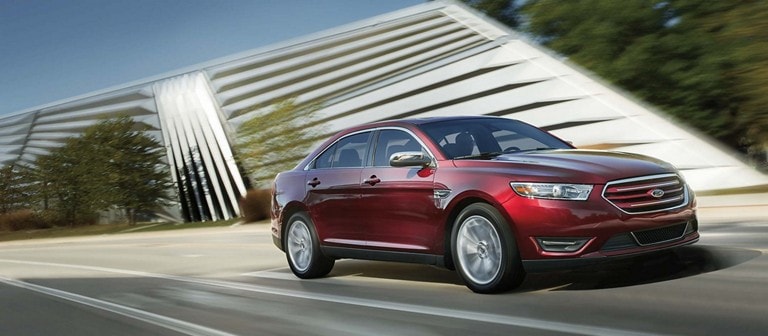 Ford Taurus Limited in Ruby Red Metallic being driven past modern art museum.