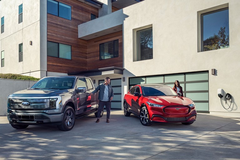A ford f 150 lightning in a driveway beside a mustang mach e