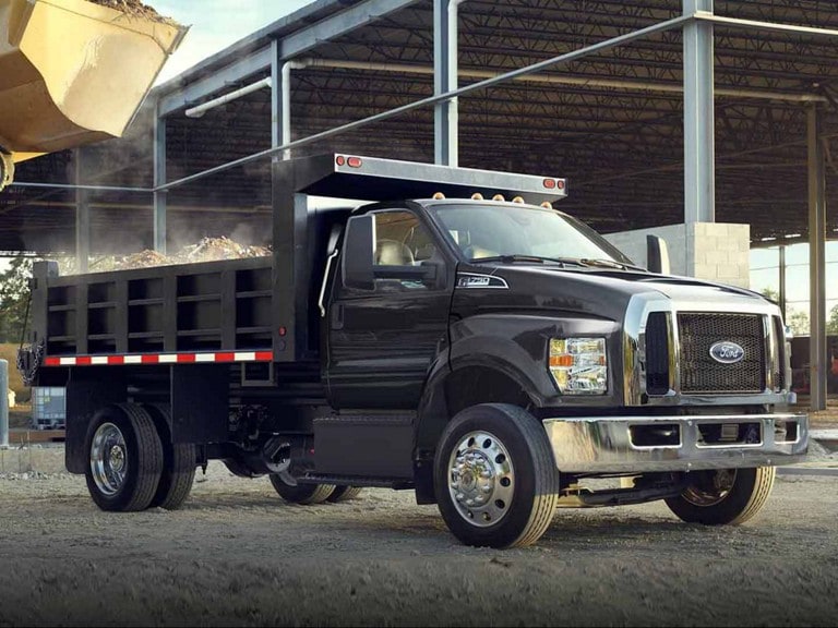 A black 2027 Ford Medium Duty truck with dump truck upfit parked in front of a construction site