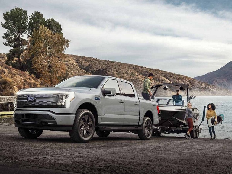 A light blue Ford F-150 Lightning® pickup truck towing a boat out of a mountain lake