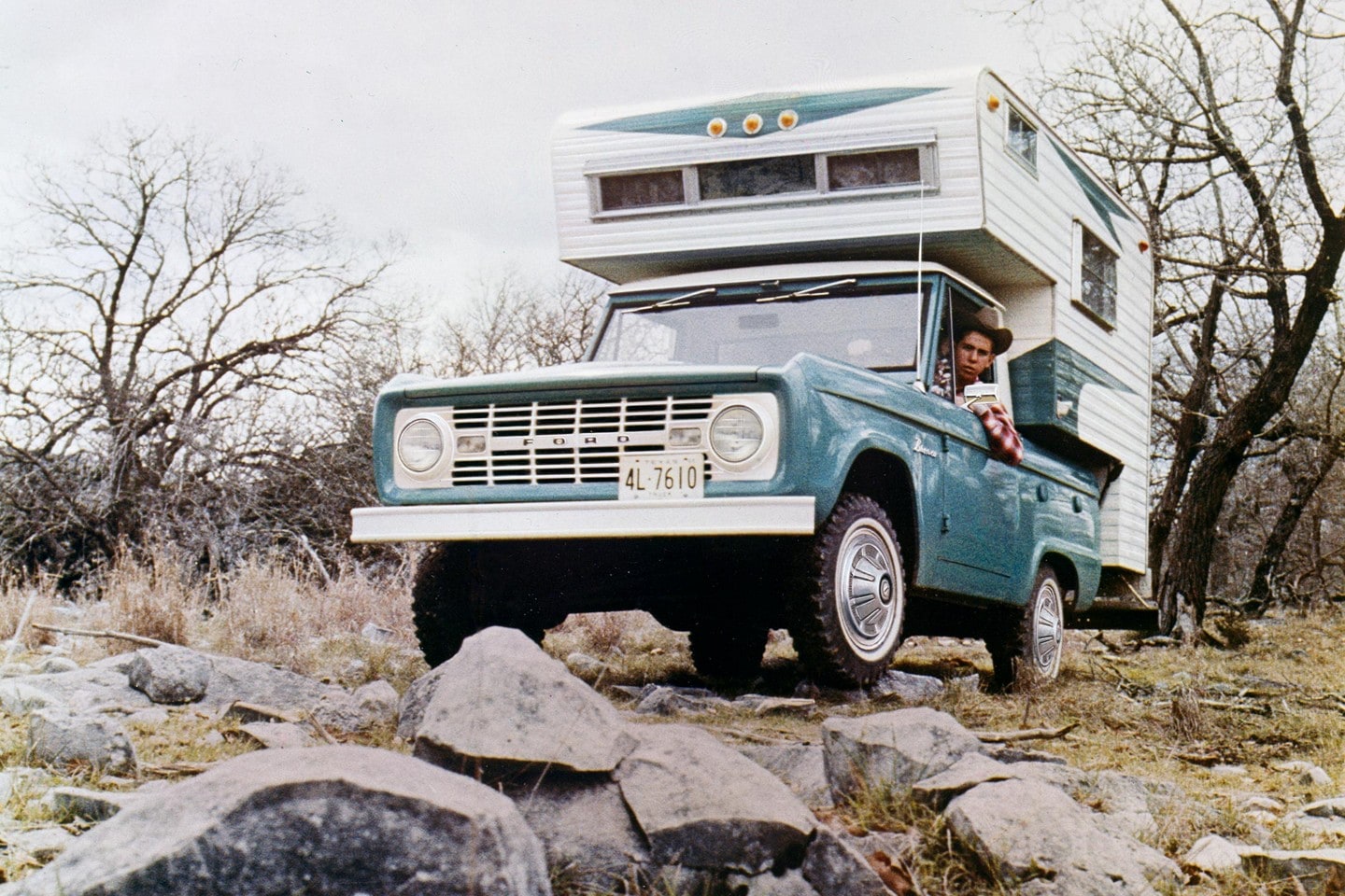 A 1967 Ford Bronco in Peacock Blue with a Camper Body driven over rocky terrain