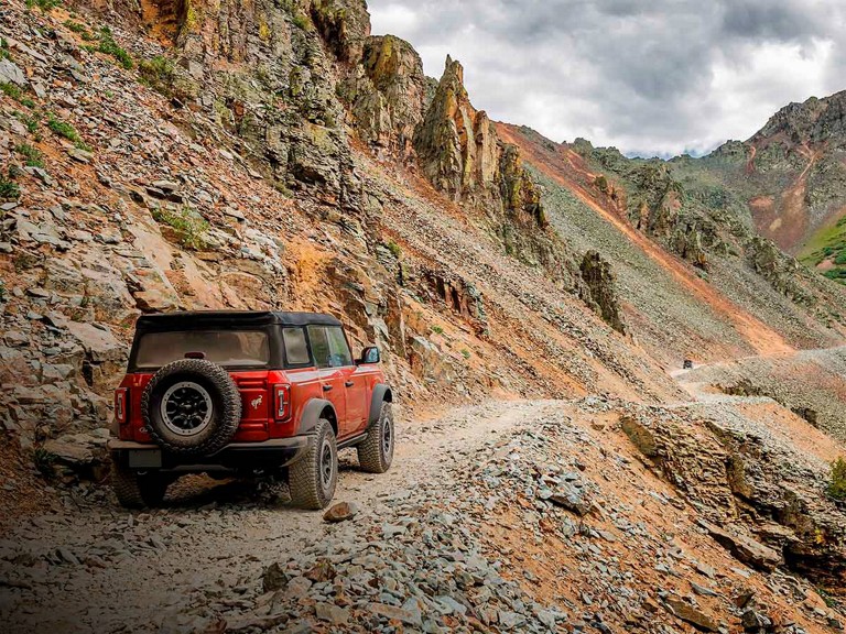 A Bronco® SUV is being driven along a rocky, two-track road through mountains