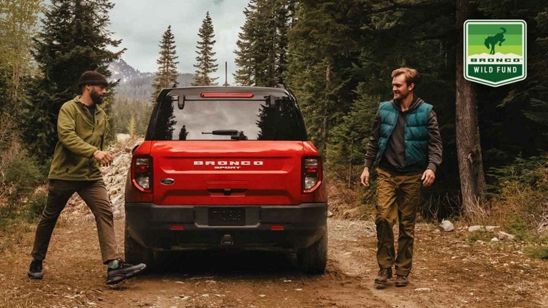 Two hikers exit a red Ford Bronco® SUV Sport parked on a woodland trail