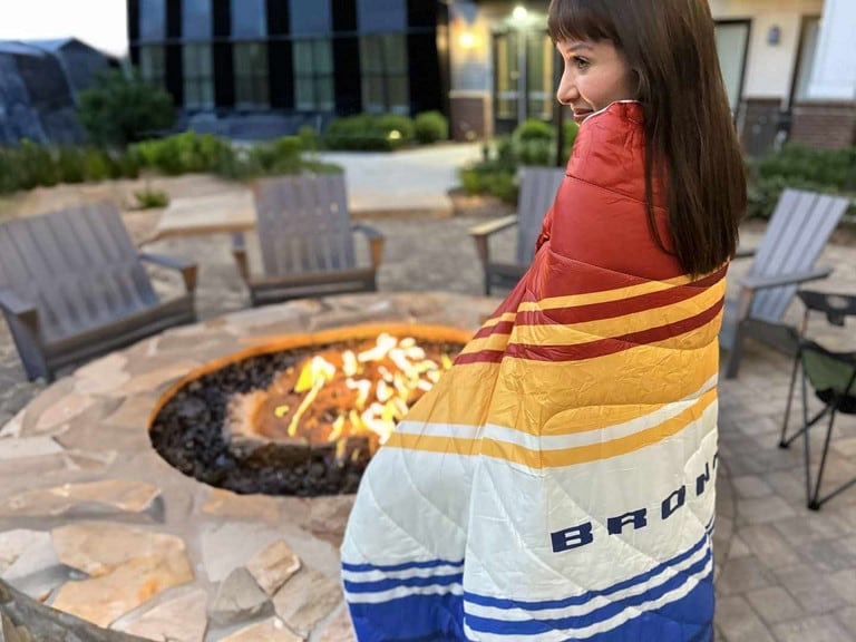 A camper being warmed by a fire, wrapped in a Bronco® nylon blanket.
