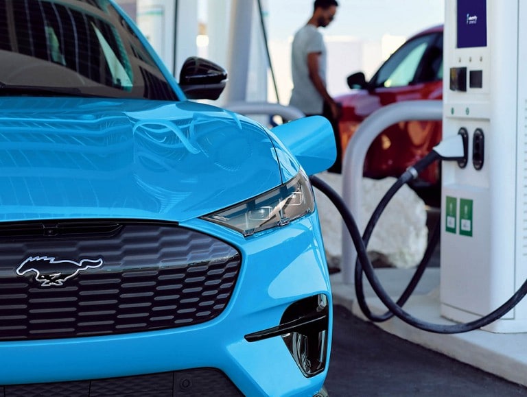A blue Ford Mustang® Mach-E® SUV parked at a charging station with optional equipment shown.