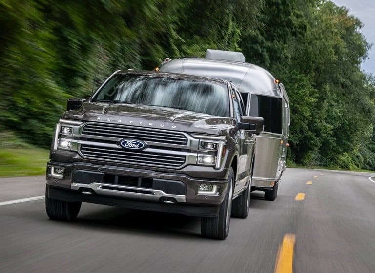 A gray Ford F-150® Platinum truck being driven on a highway while towing a silver trailer.