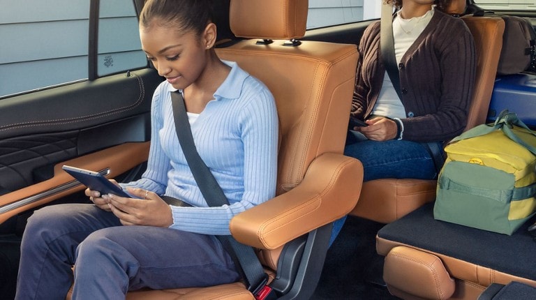 Two smiling children using mobile devices while sitting in the second and third rows of a Ford SUV.