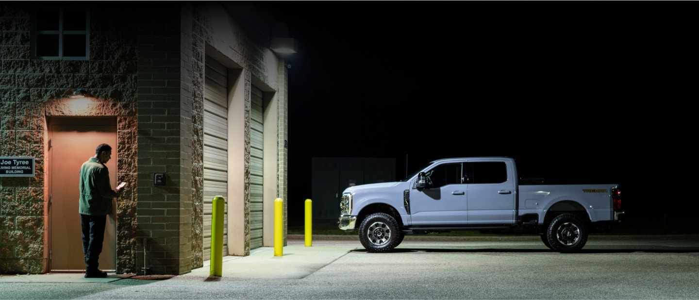 Man using phone in parking lot at night, near truck.