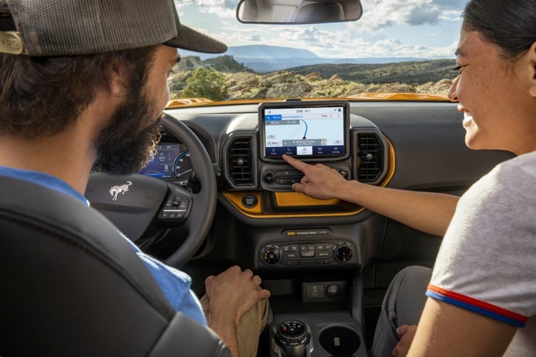 A blue Ford Mustang Mach-E® SUV being driven on a tree-lined country road surrounded by greenery.
