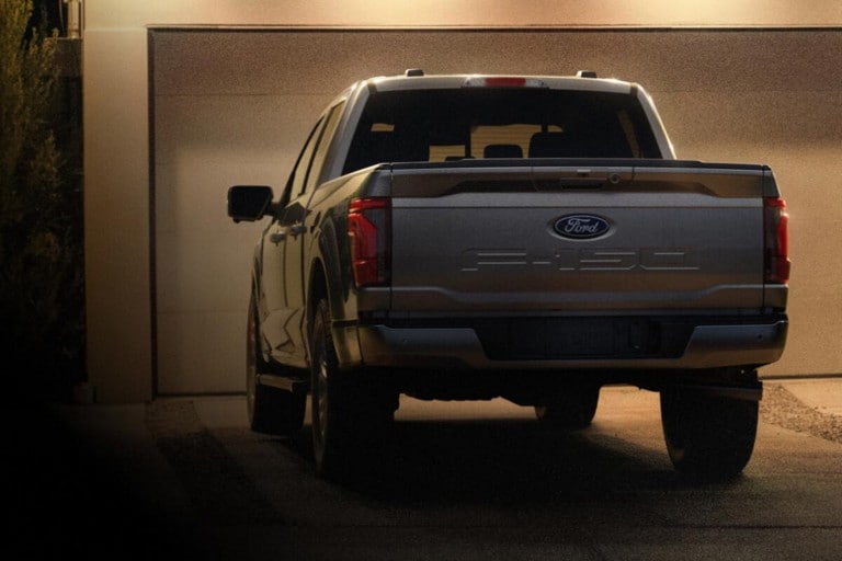 A Ford F-150® truck parked in the driveway of a modern, suburban, well-lit home at night.