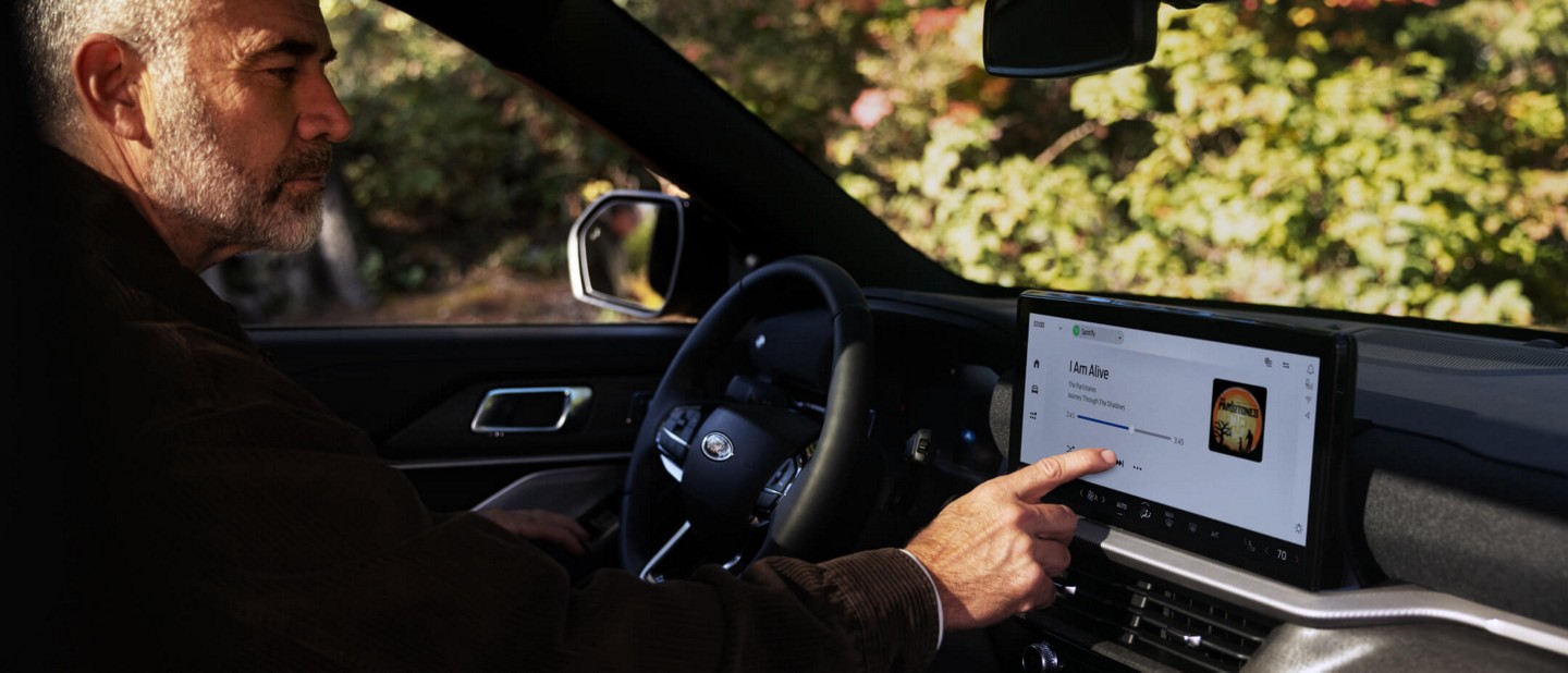 A driver sitting in a parked 2025 Ford Explorer® SUV selecting music on the technology touchscreen.