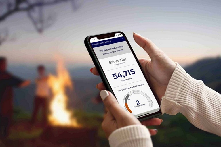 A driver holding a mobile phone device showing a FordPass Rewards Points mobile app screen.