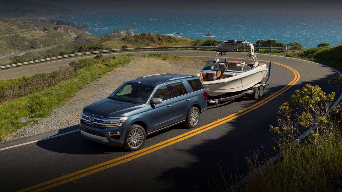 A 2024 Ford Expedition® SUV being driven up a mountain road towing a boat