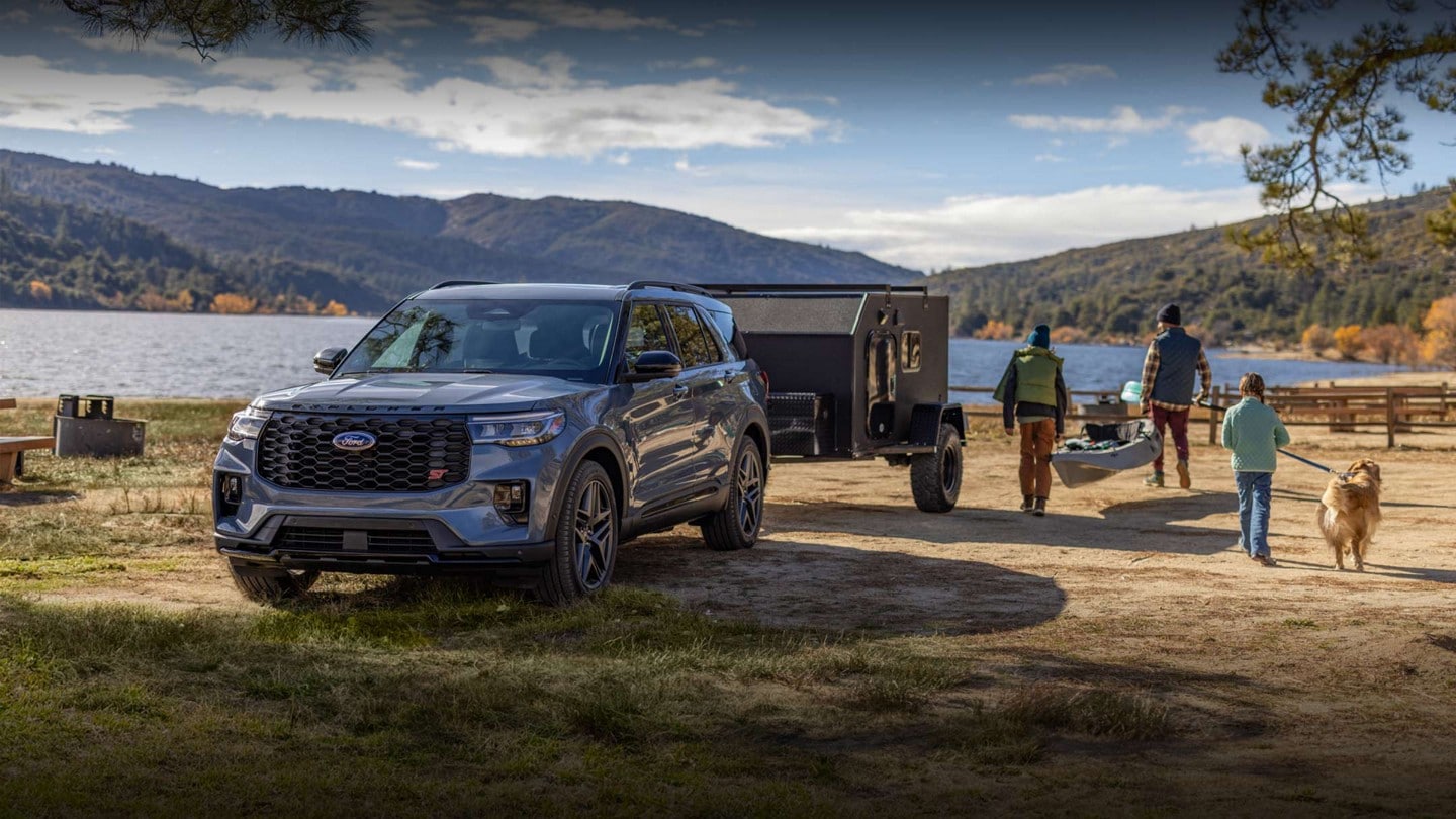 A 2024 Ford Explorer SUV® parked by a lake hooked up to a camper