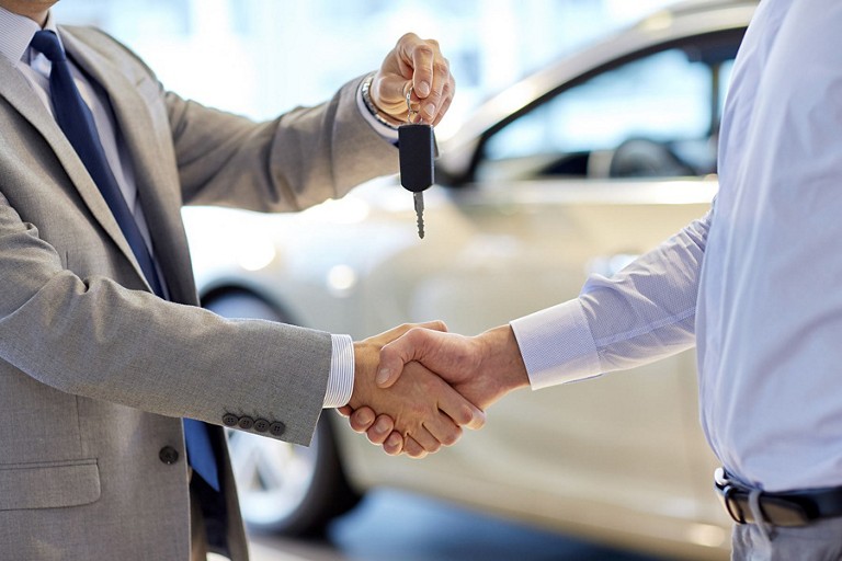 Two people shaking hands in front of a vehicle's driver's side door