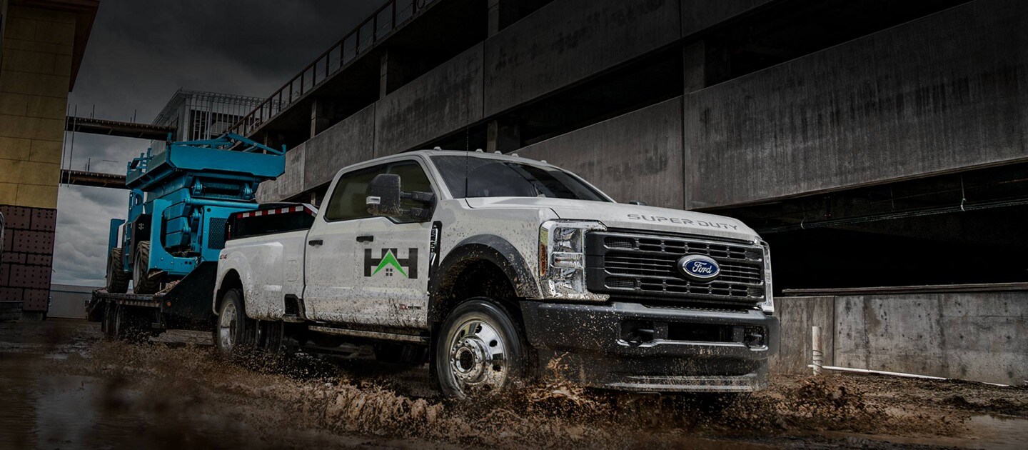 2025 Ford Super Duty® F-350® XLT DWR truck in Oxford White pulling a hydraulic lift through a large puddle of mud