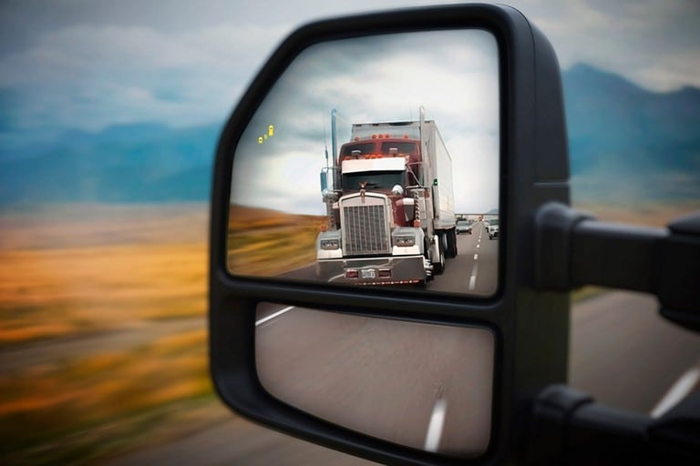 Close-up image of the side view mirror with BLIS icon and the reflection of a semi-truck