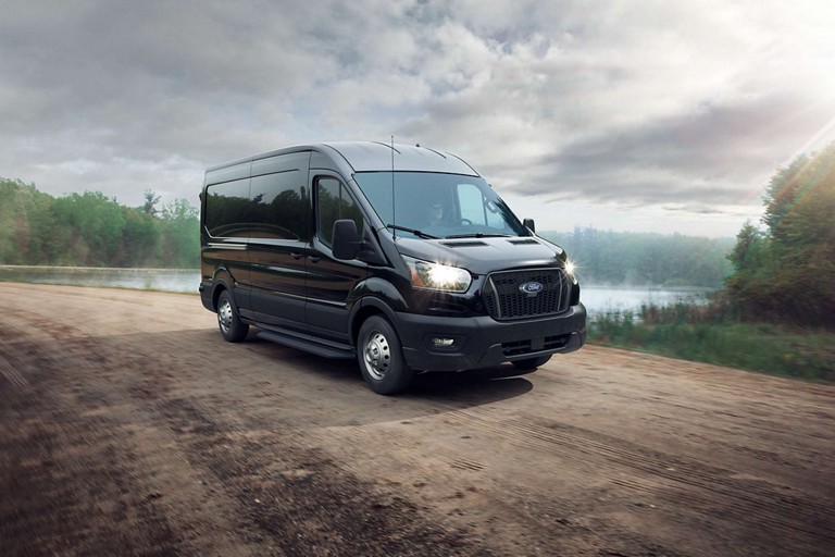 A 2025 Ford Transit® van in Agate Black with Intelligent All-Wheel-Drive travels down a dirt road