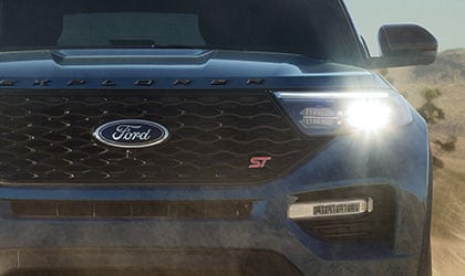 Vista frontal de una Ford Explorer S T 2020 en Blue Metallic andando por un camino desértico lleno de polvo