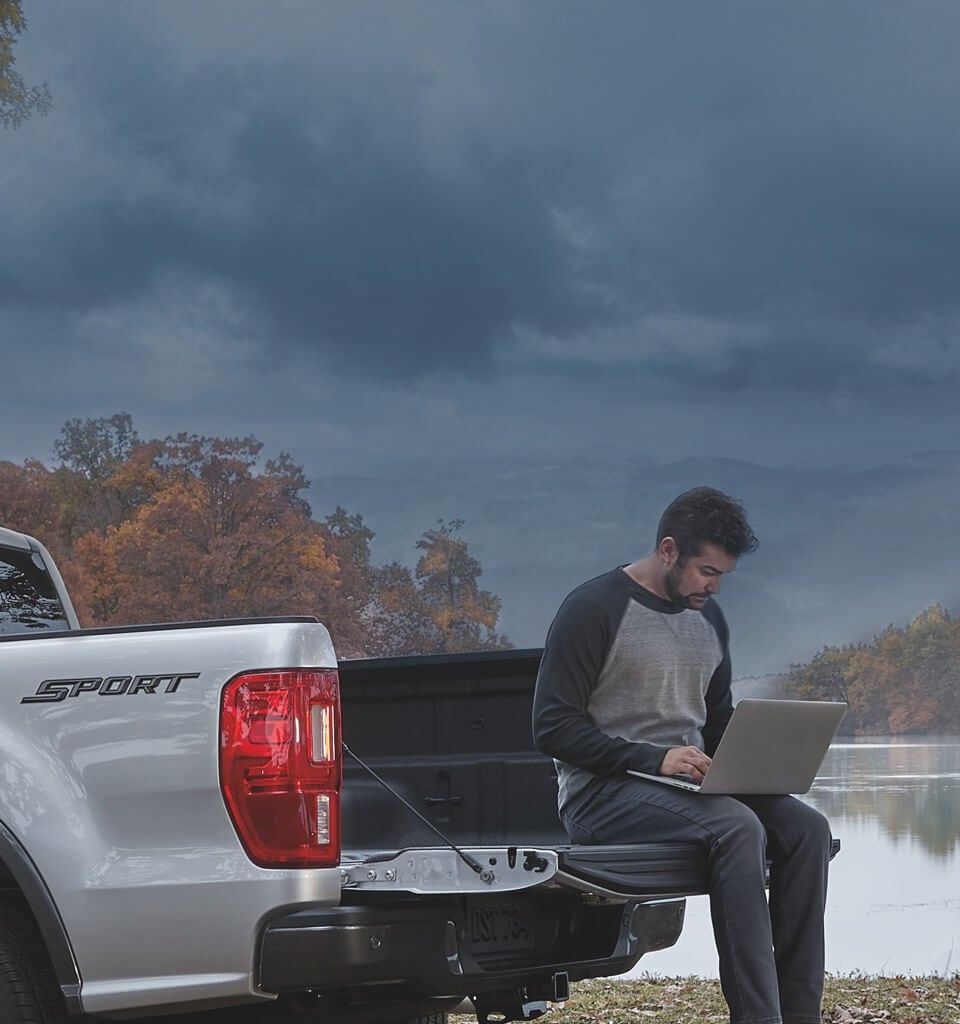 Hombre usando laptop mientras está sentado en la plataforma de una camioneta Ford Ranger Lariat 2020 estacionada cerca de un lago