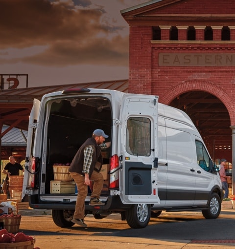  People unloading produce from two 2021 Ford Transit vans in  front of a market