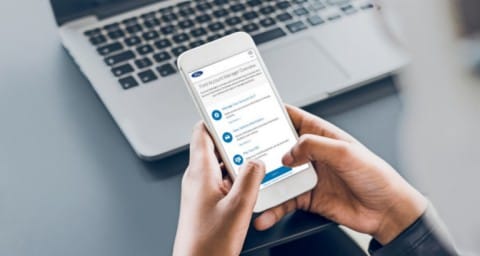 Close up on hands holding mobile phone displaying the Ford Credit website with laptop in background