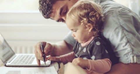 Persona trabajando desde casa en frente de una laptop con bebé en la falda