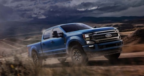 2020 Ford Super Duty Crew Cab in Velocity Blue being driven uphill on dirt road in desert