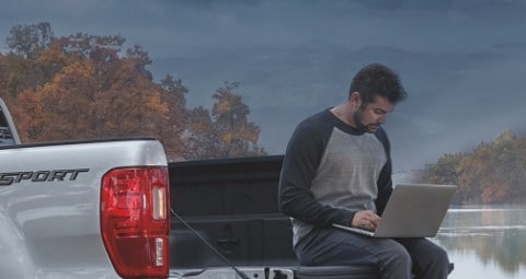 Hombre usando laptop mientras está sentado en la plataforma de una camioneta Ford Ranger Lariat 2020 estacionada cerca de un lago