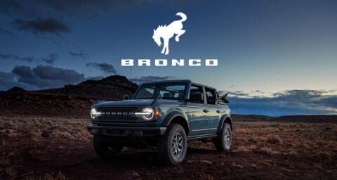 A 2022 Ford Bronco is parked in the desert as the sun sets behind it.