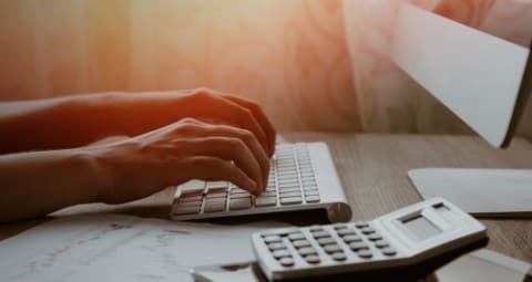 Person working with hands on computer keyboard with a calculator to the right. 