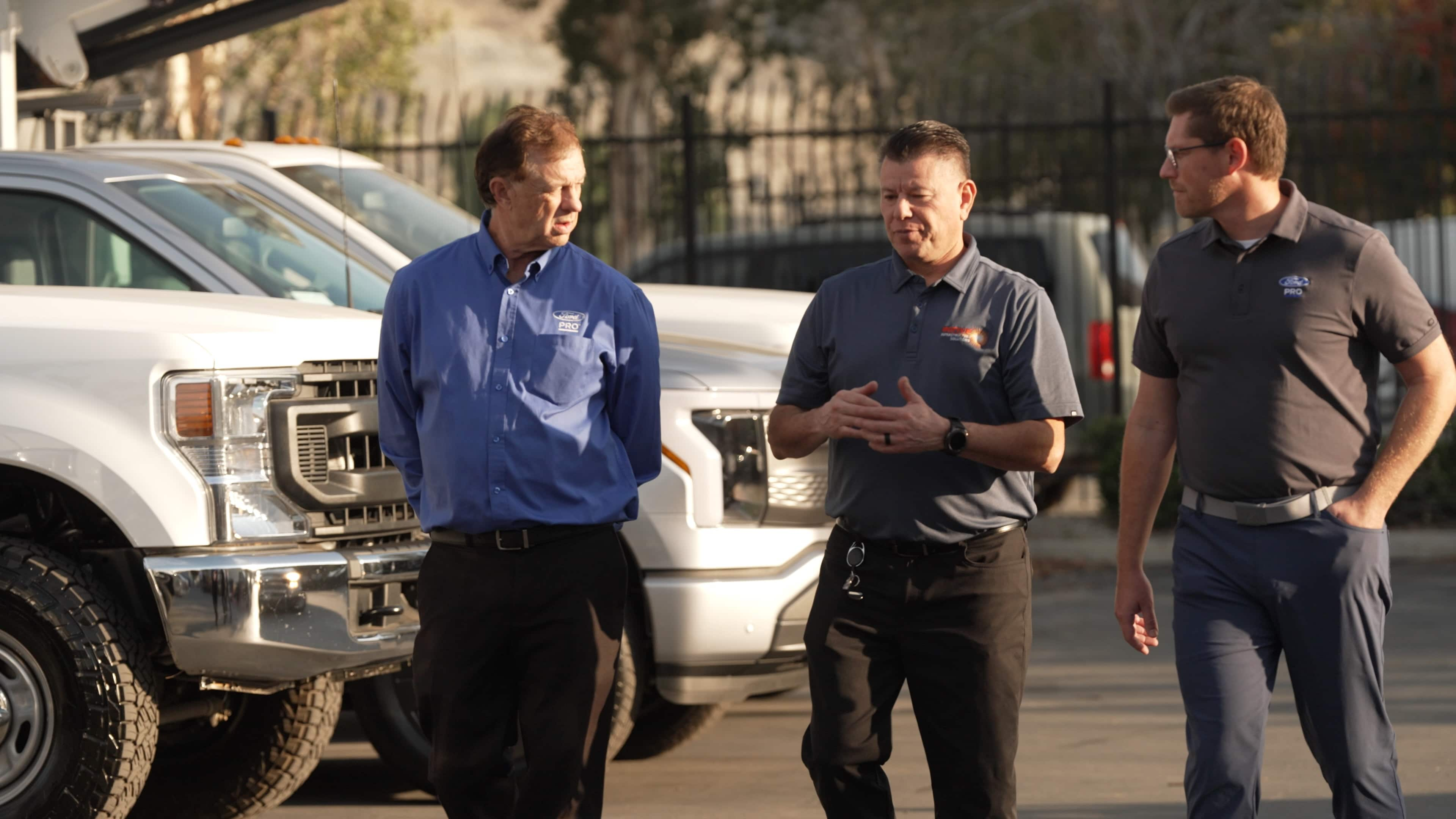 Two Ford pro representatives speaking with a business owner as they walk past commercial ford vehicles