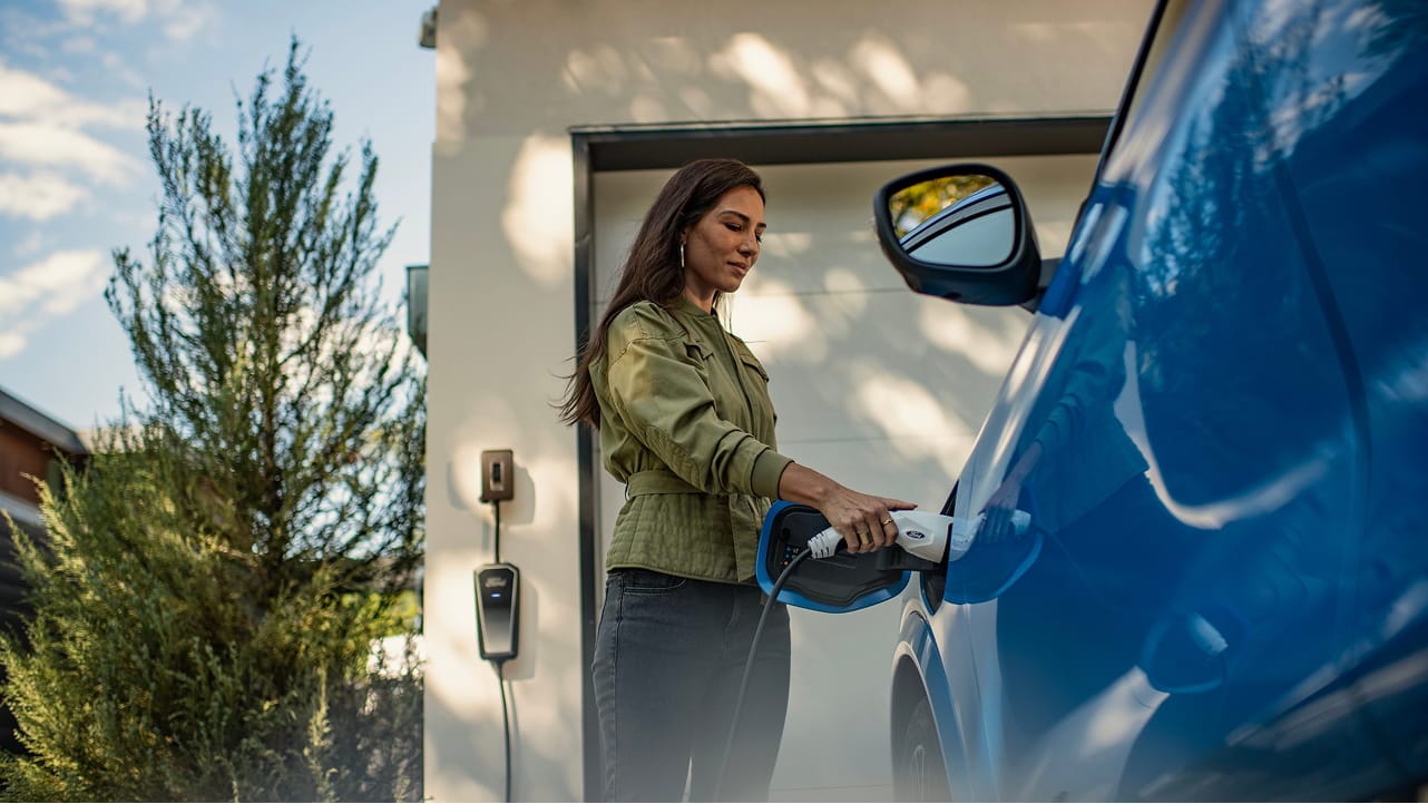 Une femme connectant un chargeur à son véhicule Ford EV.