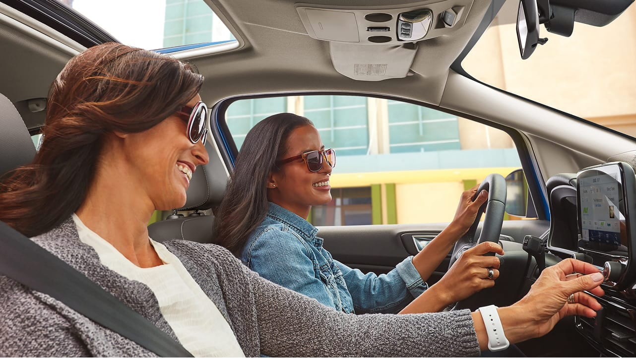 Two women smiling while sitting inside a Ford vehicle. 
