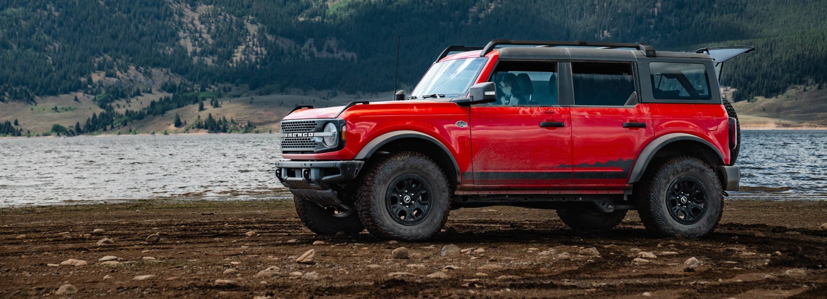 A red Ford Bronco parked next to a lake.