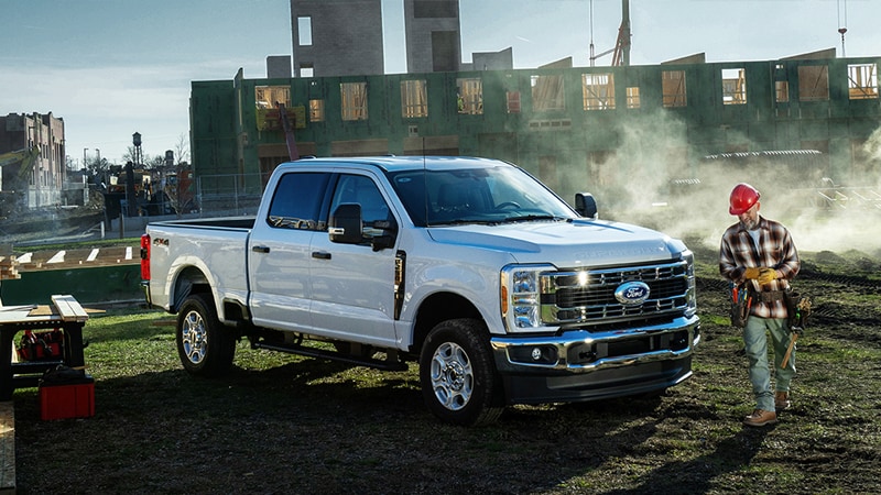 White Ford Super Duty pickup truck parked at a work site near a person wearing a hard hat.