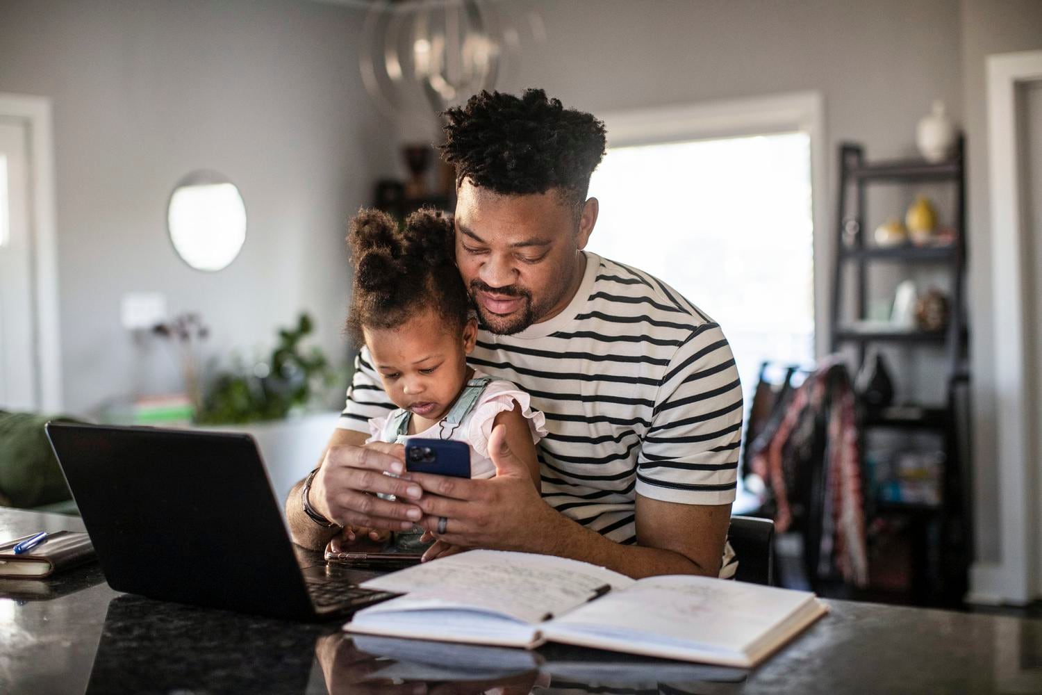 A father holding his infant daughter in his lap while he checks his mobile device. 