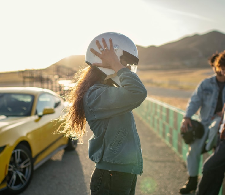 Woman removing helment in front of yellow vehicle