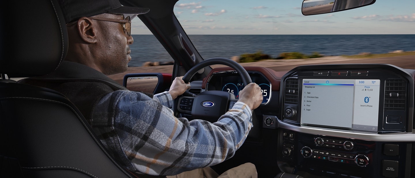 A person behind a wheel driving a 2022 Ford F150® with the ocean in the background